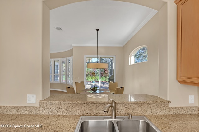 kitchen featuring light stone counters, sink, decorative light fixtures, and crown molding