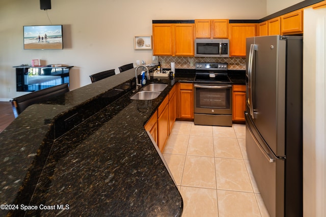 kitchen with sink, appliances with stainless steel finishes, tasteful backsplash, dark stone counters, and light tile patterned floors