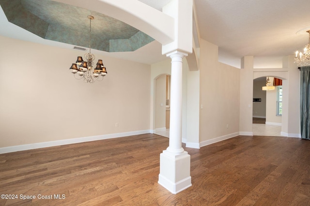 unfurnished room featuring ornate columns, hardwood / wood-style floors, a notable chandelier, and a raised ceiling