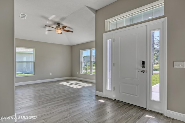 foyer entrance with ceiling fan, a textured ceiling, light hardwood / wood-style flooring, and vaulted ceiling