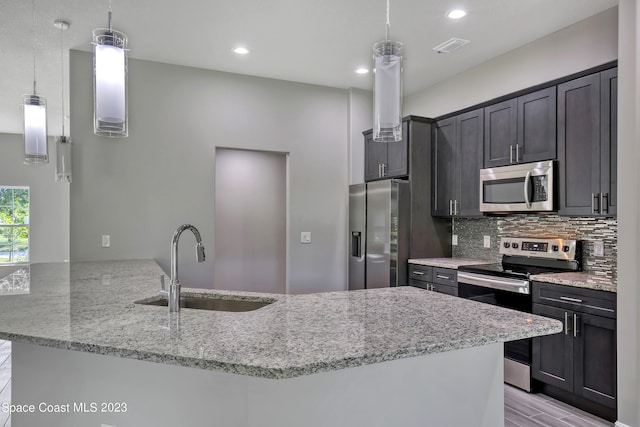 kitchen featuring stainless steel appliances, sink, kitchen peninsula, light stone counters, and decorative light fixtures