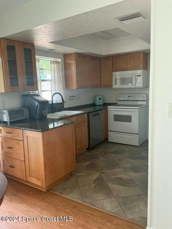 kitchen featuring hardwood / wood-style flooring, sink, tasteful backsplash, dark stone countertops, and white appliances