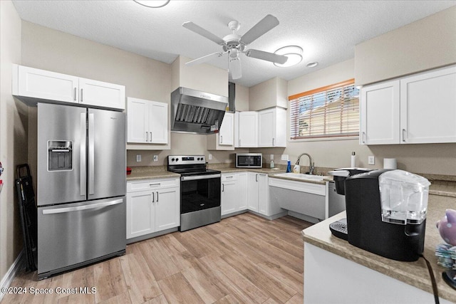 kitchen featuring stainless steel appliances, white cabinetry, sink, wall chimney range hood, and light wood-type flooring