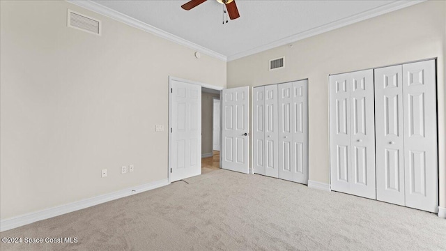 unfurnished bedroom featuring ceiling fan, multiple closets, crown molding, and light colored carpet