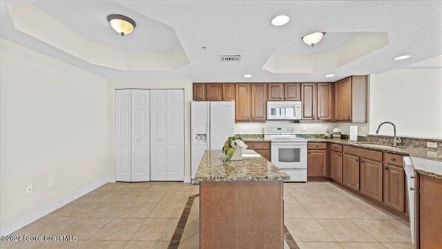 kitchen with sink, white appliances, a tray ceiling, and light stone countertops