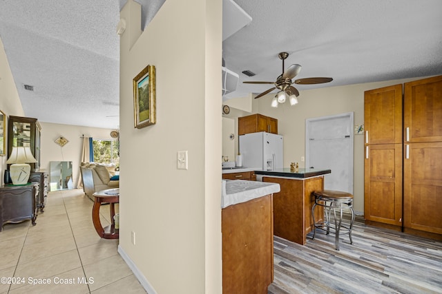 kitchen featuring white refrigerator with ice dispenser, a kitchen island, a textured ceiling, a breakfast bar, and light hardwood / wood-style flooring