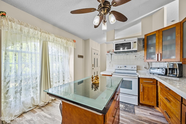 kitchen with tasteful backsplash, ceiling fan, white appliances, a center island, and light wood-type flooring