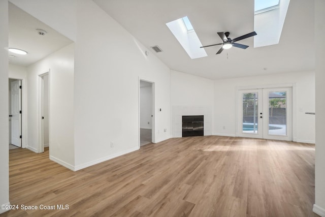 unfurnished living room featuring french doors, high vaulted ceiling, a tiled fireplace, light hardwood / wood-style floors, and ceiling fan