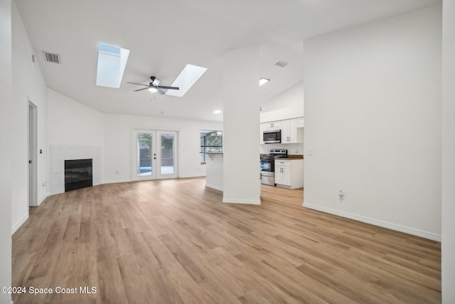 unfurnished living room with high vaulted ceiling, a skylight, a fireplace, light hardwood / wood-style flooring, and french doors