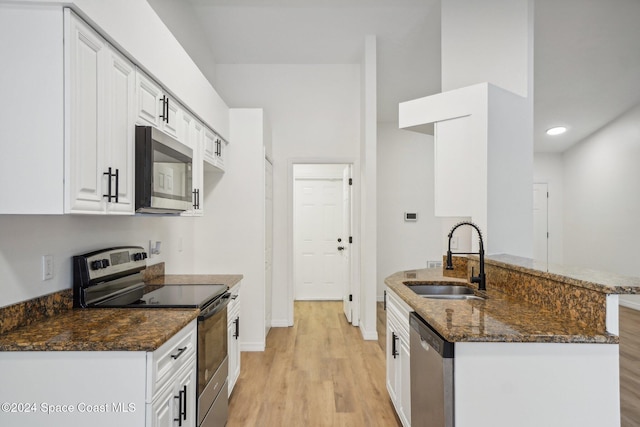 kitchen with dark stone counters, white cabinetry, appliances with stainless steel finishes, light wood-type flooring, and sink