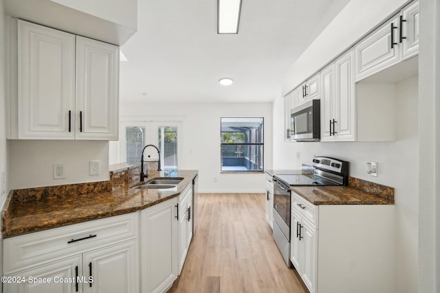 kitchen with light hardwood / wood-style floors, white cabinets, sink, appliances with stainless steel finishes, and dark stone countertops