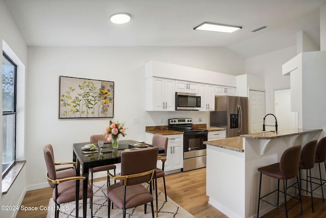 kitchen featuring stainless steel appliances, light wood-type flooring, vaulted ceiling, white cabinets, and kitchen peninsula