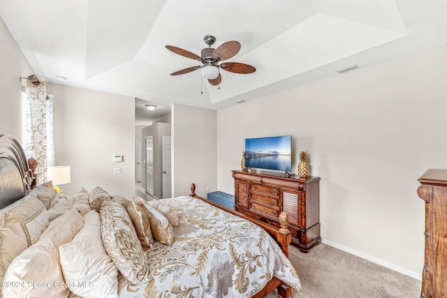 bedroom featuring a tray ceiling, light carpet, and ceiling fan