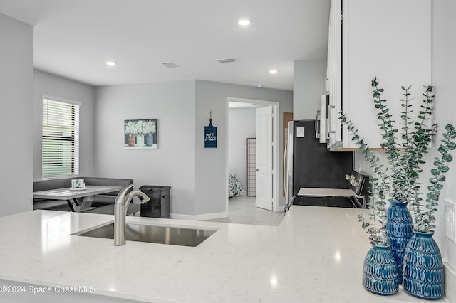 kitchen with white cabinets, stainless steel appliances, sink, and light stone countertops