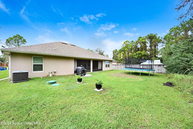 back of property featuring central AC unit, a yard, and a trampoline