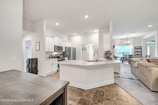 kitchen with light stone counters, stainless steel appliances, a notable chandelier, sink, and white cabinets