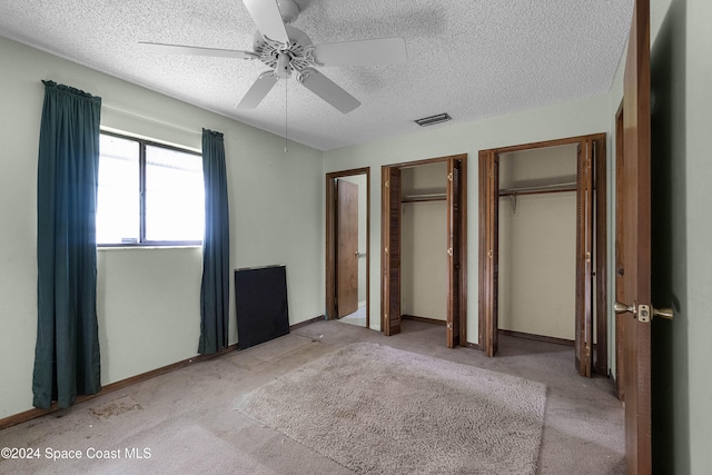 unfurnished bedroom featuring a textured ceiling, two closets, ceiling fan, and light colored carpet