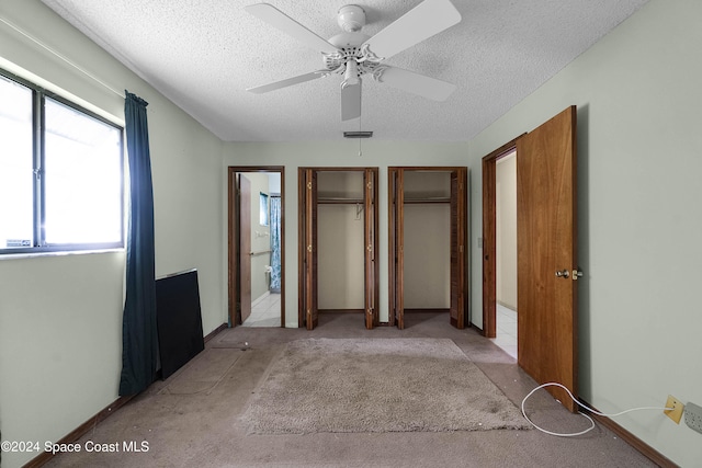 unfurnished bedroom featuring multiple closets, ceiling fan, light carpet, and a textured ceiling