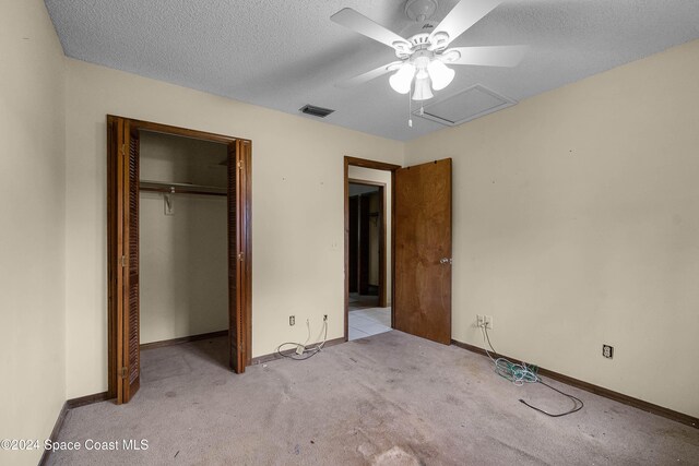 unfurnished bedroom featuring ceiling fan, light colored carpet, a textured ceiling, and a closet