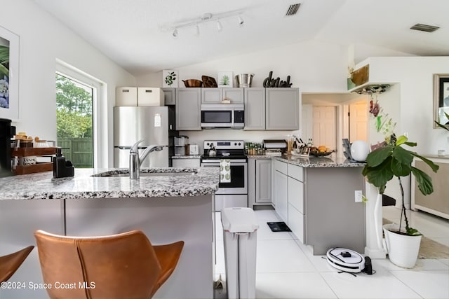 kitchen featuring stainless steel appliances, vaulted ceiling, gray cabinetry, and light stone counters