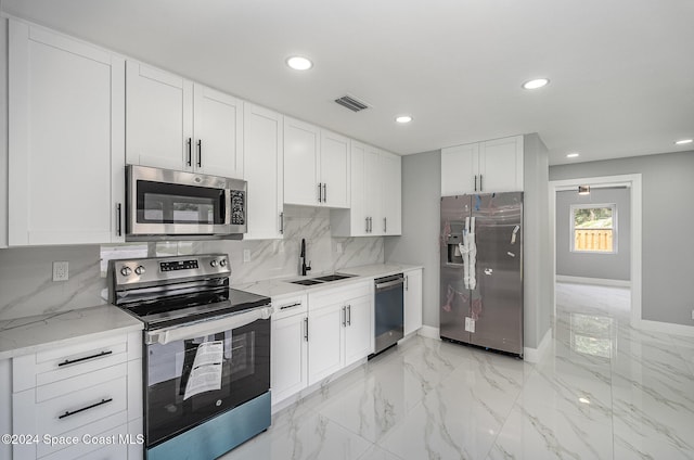 kitchen with sink, tasteful backsplash, light stone countertops, white cabinetry, and appliances with stainless steel finishes