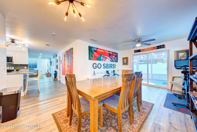 dining area with a textured ceiling, light hardwood / wood-style floors, and ceiling fan with notable chandelier