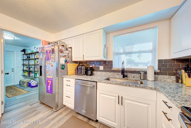 kitchen featuring white cabinets, sink, tasteful backsplash, light wood-type flooring, and appliances with stainless steel finishes