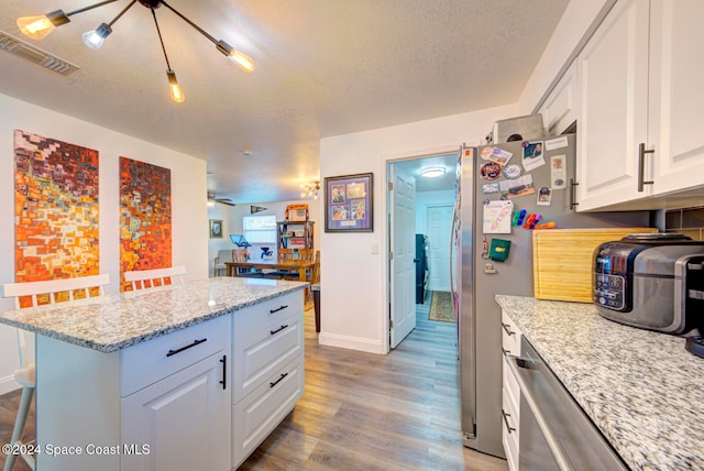 kitchen featuring light stone counters, light wood-type flooring, a textured ceiling, a kitchen bar, and white cabinets