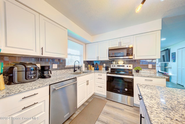 kitchen with light hardwood / wood-style floors, stainless steel appliances, decorative backsplash, sink, and white cabinetry