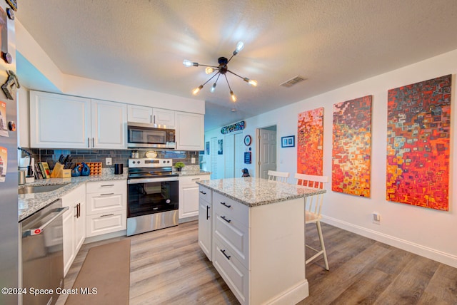 kitchen with stainless steel appliances, white cabinets, light hardwood / wood-style flooring, and a center island