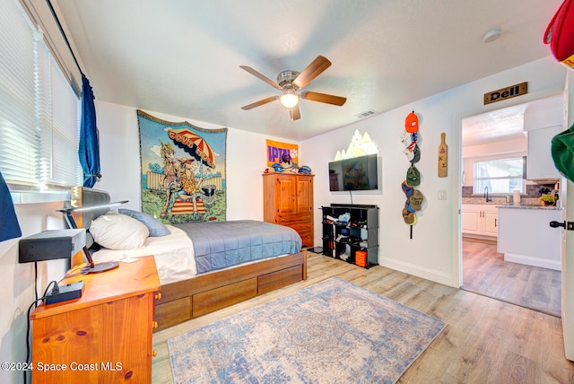 bedroom with ensuite bathroom, light hardwood / wood-style floors, ceiling fan, and sink