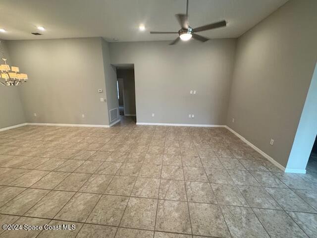 spare room featuring ceiling fan with notable chandelier