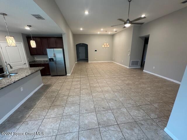 kitchen featuring light stone counters, decorative light fixtures, dark brown cabinets, stainless steel refrigerator with ice dispenser, and ceiling fan with notable chandelier