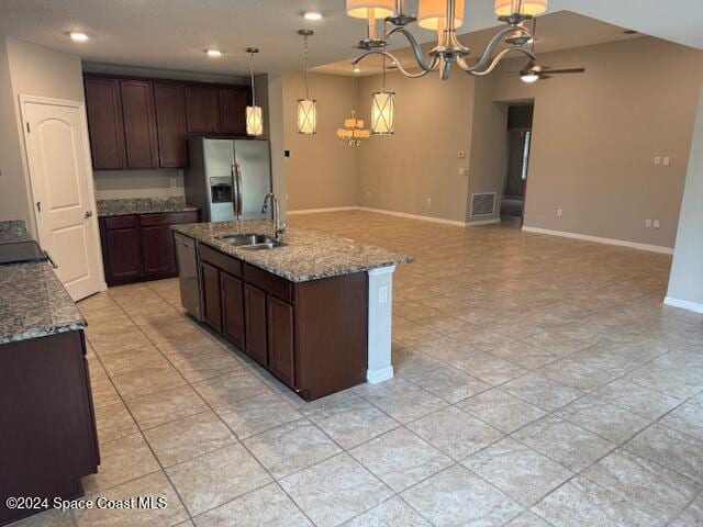 kitchen with a center island with sink, dark brown cabinetry, light stone countertops, decorative light fixtures, and stainless steel fridge