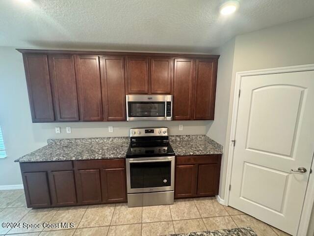 kitchen with dark brown cabinetry, light stone counters, appliances with stainless steel finishes, a textured ceiling, and light tile patterned floors