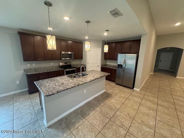 kitchen with stainless steel appliances, sink, hanging light fixtures, an island with sink, and dark brown cabinets