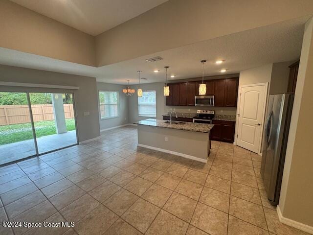 kitchen featuring a center island with sink, light tile patterned floors, decorative light fixtures, and appliances with stainless steel finishes