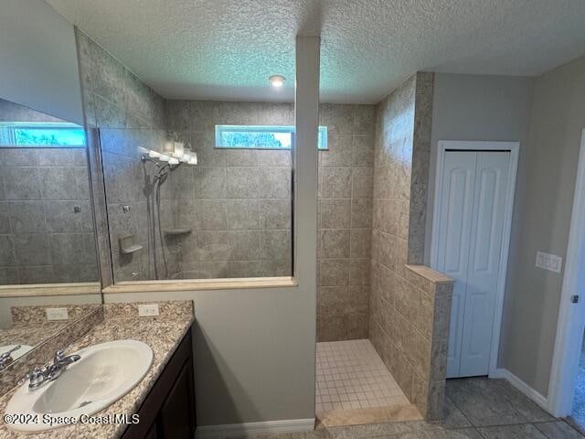 bathroom featuring a tile shower, vanity, a textured ceiling, and tile patterned floors