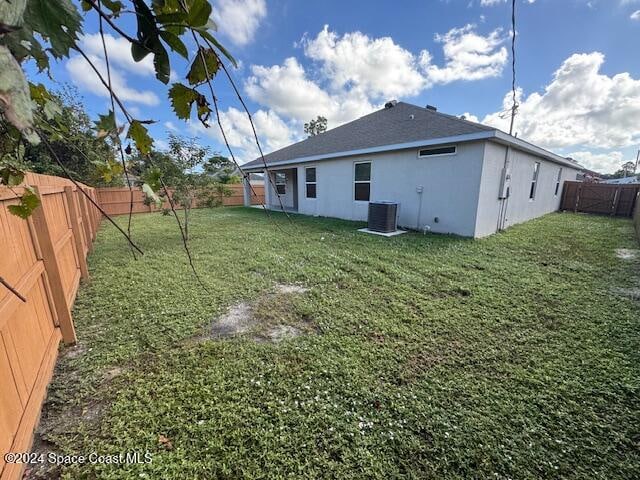 rear view of property with central AC unit and a yard