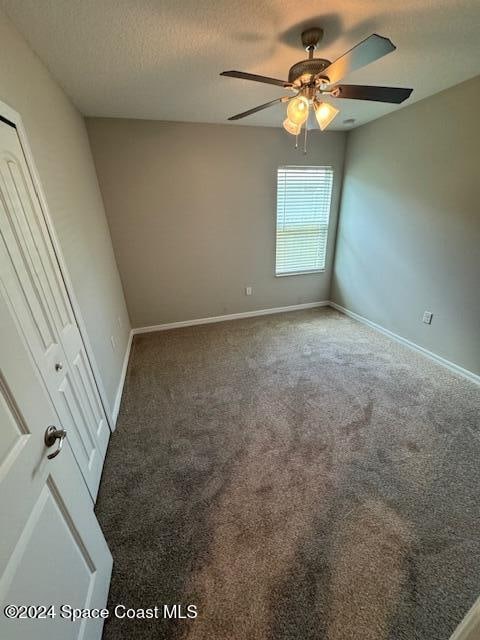 spare room with a textured ceiling, dark colored carpet, and ceiling fan