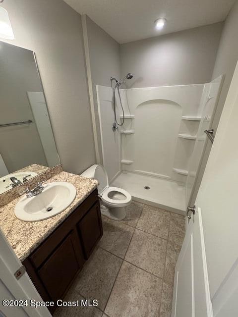 bathroom with toilet, a shower, vanity, and tile patterned floors