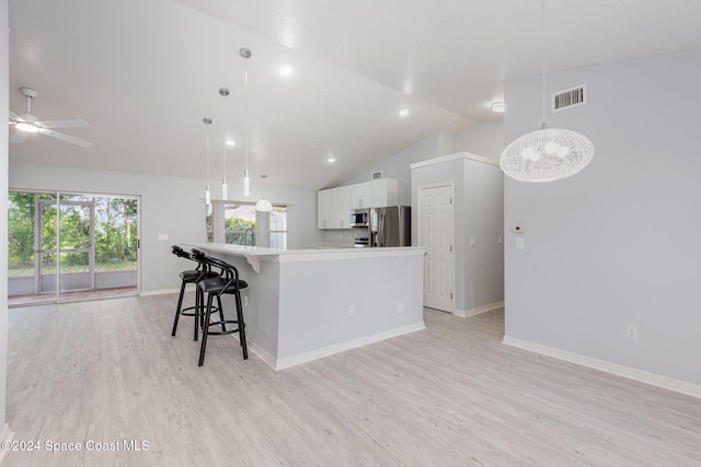 kitchen with stainless steel appliances, white cabinetry, decorative light fixtures, vaulted ceiling, and light hardwood / wood-style flooring