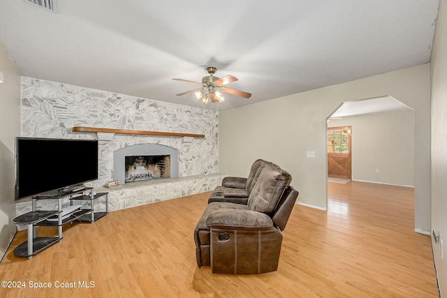 living room featuring hardwood / wood-style flooring, ceiling fan, and a stone fireplace