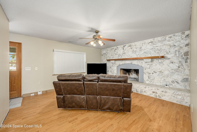 living room with hardwood / wood-style floors, ceiling fan, a stone fireplace, and a textured ceiling