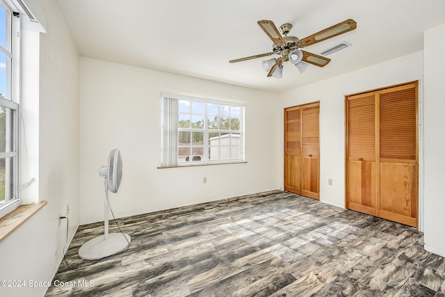 unfurnished bedroom with multiple closets, ceiling fan, and dark hardwood / wood-style flooring