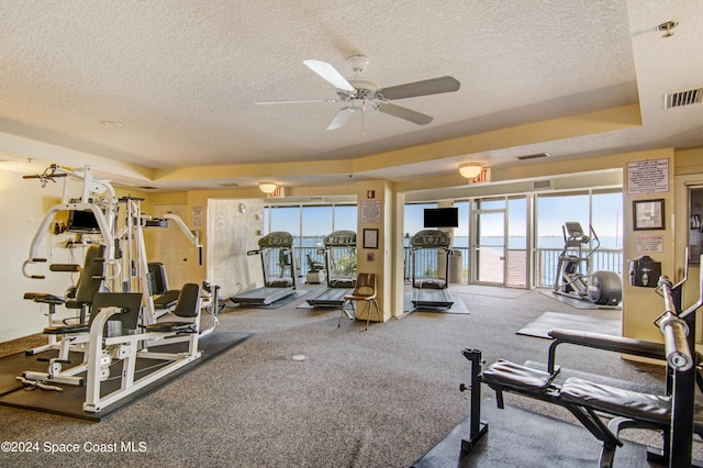 gym featuring carpet flooring, ceiling fan, a tray ceiling, and a textured ceiling