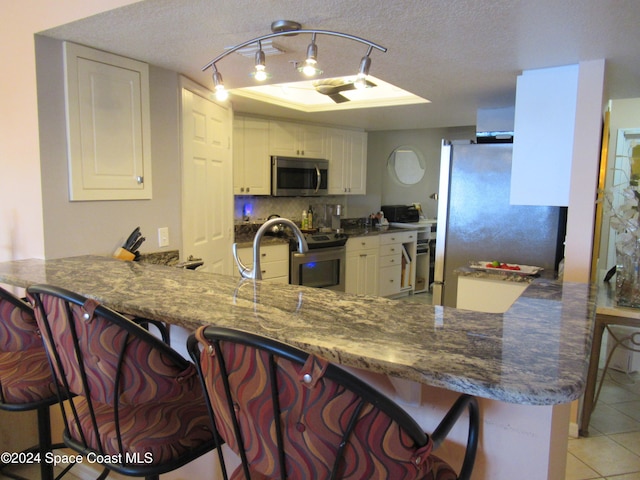 kitchen with a kitchen bar, white cabinetry, light tile patterned floors, kitchen peninsula, and stainless steel appliances