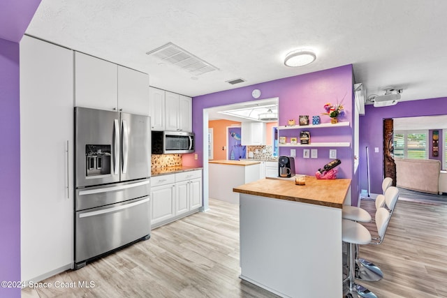 kitchen with white cabinets, backsplash, stainless steel appliances, and wood counters