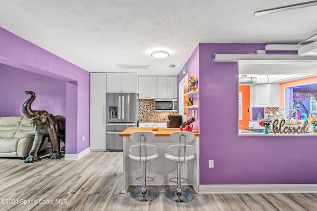 kitchen with stainless steel appliances, tasteful backsplash, butcher block countertops, a kitchen bar, and white cabinets