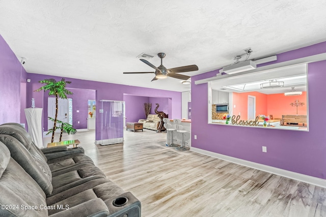 living room with a textured ceiling, light wood-type flooring, and ceiling fan